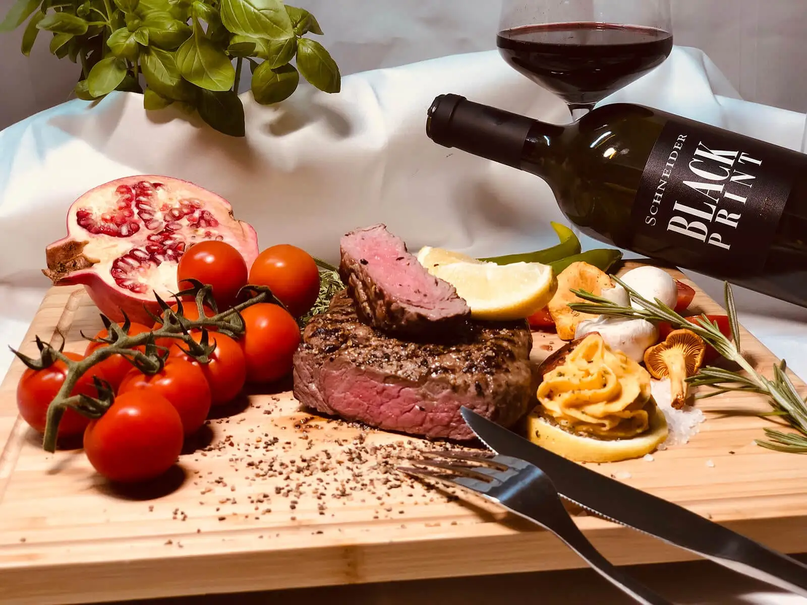 Angeschnittenes Rinderfilet auf einem Holzbrett mit Kräuterbutter, Tomaten und Pilzen