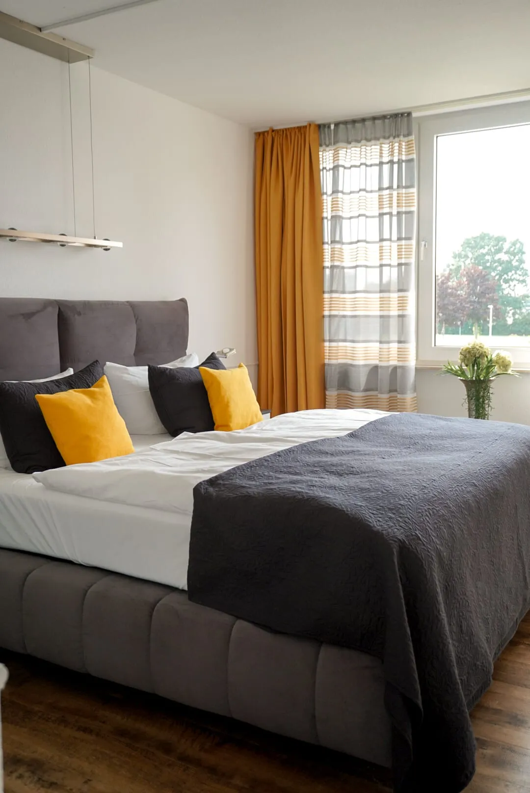 Doppelzimmer de luxe mit Boxspringbett, gelben Kissen und senfgelbem Vorhang am Fenster